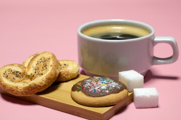 Chocolate chip cookies, refined sugar and a cup of coffee on a pink background.