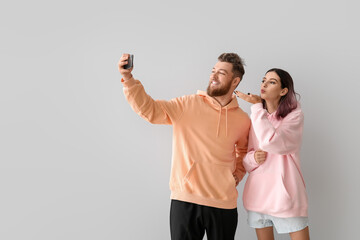 Cool young couple in hoodies taking selfie on light background