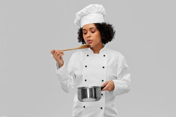 culinary and people concept - female chef in toque with saucepan and spoon cooking and tasting food...