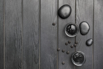 Bowls of activated carbon facial mask, pills and spa stones on dark wooden background
