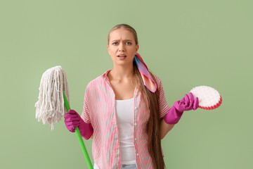 Displeased young woman with sponge and floor mop on color background