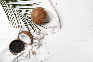 Coconut shell with activated carbon and palm leaf on white wooden background