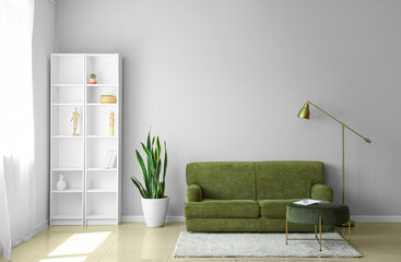 Interior of light living room with green sofa, pouf and shelving unit