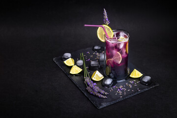 Fresh homemade lemonade with lavender and ice. Delicious purple icy cold party drink on slate board with dark background.