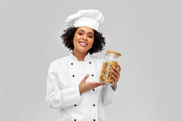 cooking, culinary and people concept - happy smiling female chef holding jar with pasta over grey background