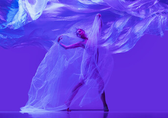 Portrait of beautiful flexible woman, ballerina dancing with cloth on purple studio background in neon. Fashion, style, art, beauty