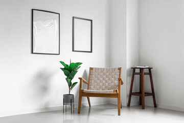 Modern armchair, houseplant and blank photo frames on wall in light room interior