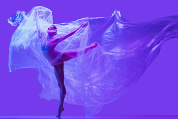 Portrait of beautiful flexible woman, ballerina dancing with cloth on purple studio background in neon. Fashion, style, art, beauty