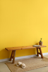 Wooden bench with magazines, flowerpot and slippers near yellow wall