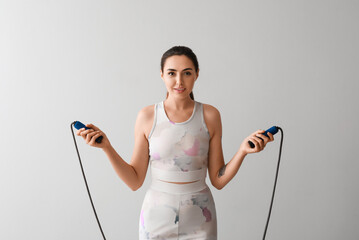 Sporty young woman with skipping rope on grey background