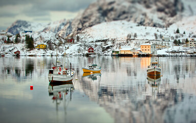 Landscape of boats on the sea surrounded by rocky mountains covered in the snow in Lofoten, Norway