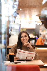 Pretty young woman with newspaper sitting at table in cafe