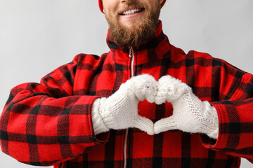 Young man making heart shape with his hands in warm gloves on light background