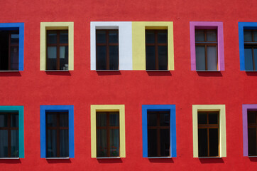 Building in the center of  city with red color painted wall and different colors paynted widows.