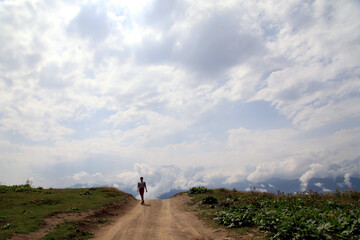 Person walking down a hill under the cloudy blue sky