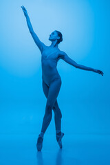 Fototapeta na wymiar Grace. Young and graceful ballet dancer isolated on blue studio background in neon light. Art, flexibility, inspiration concept.