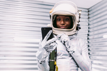 Black astronaut browsing smartphone in spaceship