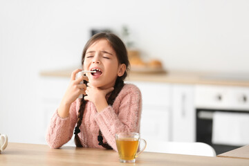 Little girl with sore throat using medical spray in kitchen