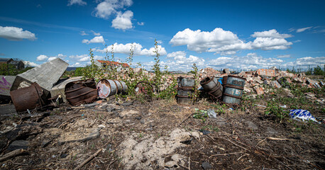 View of rusty barrels in junkyard against blue sky with clouds in a bright sunlight