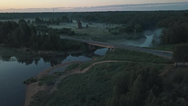 An early foggy morning in the countryside outside the city. Lone car, road, bridge, church, fog, forest around