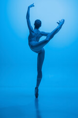 Back view of young and graceful ballet dancer isolated on blue studio background in neon light. Art, motion, action, flexibility, inspiration concept.
