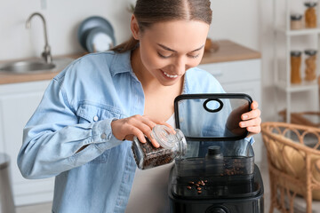Fototapeta na wymiar Young woman putting beans into coffee machine in kitchen, closeup