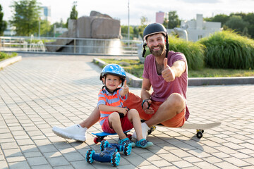 Happy father and son in helmets play in the Park with a robot car that is controlled by a glove while sitting on skateboards.