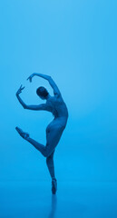 Fototapeta na wymiar Grace. Young and graceful ballet dancer isolated on blue studio background in neon light. Art, flexibility, inspiration concept.