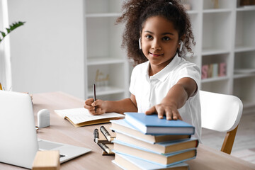 Little African-American girl with earphones and books studying online at home