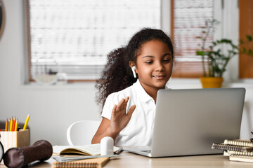 Little African-American girl in earphones studying with online tutor at home