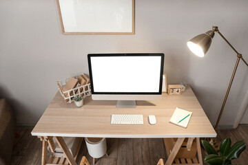 Comfortable workplace with modern computer and glowing lamp near grey wall