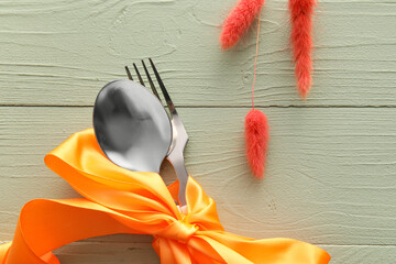 Elegant cutlery and ribbon on green wooden background