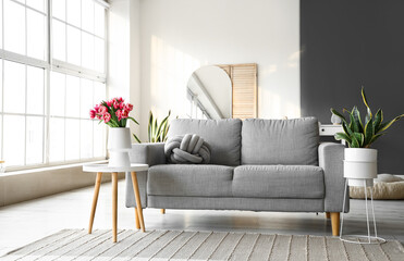 Vase with tulip flowers on small table and sofa in living room
