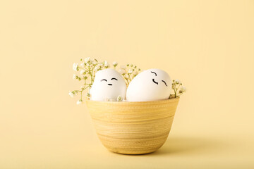 Bowl with creative Easter eggs and flowers on beige background
