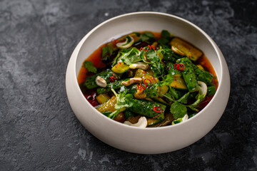 Chinese Smashed Cucumber salad, pai huang gua, sprinkled with fresh coriander leaves in a black bowl with chopsticks on a concrete table, close-up, horizontal view from above