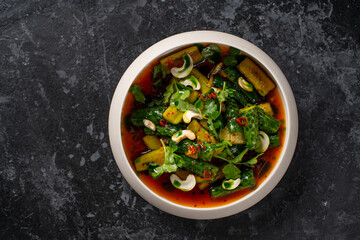 Chinese Smashed Cucumber salad, pai huang gua, sprinkled with fresh coriander leaves in a black bowl with chopsticks on a concrete table, close-up, horizontal view from above
