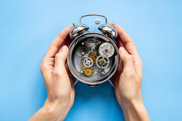 Hands holding alarm clock mechanism with steel gears and wheels close up