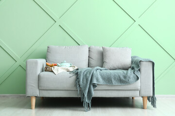 Tray with teapot on stylish sofa near green wall