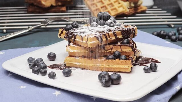 weiche, zarte belgische Waffeln mit frischen Blaubeeren und Schokoladensauce, bestreut mit s&uuml;ssem Puderzucker auf einem weissen Teller