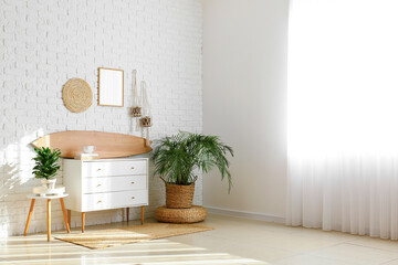 Interior of light room with wooden surfboard, commode and houseplants