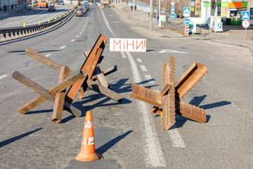 Protective anti-tank metal welded hedgehogs on the carriageway of the city road and the inscription Mines on a sunny day. - obrazy, fototapety, plakaty