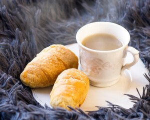 A cup of coffee and delicious croissants on a fluffy blanket