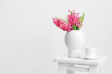 Vase with hyacinth flowers and cup on stool near white wall