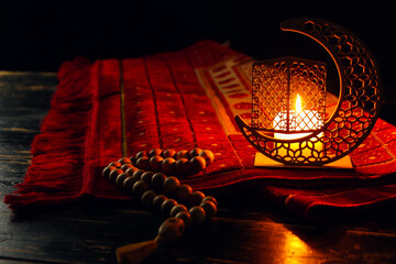 Arabic candle holder with glowing candle, carpet and tasbih on dark background