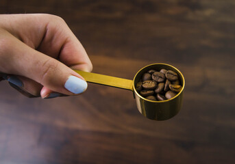 Photo of a woman's hand with a light nail polish and holding a coffee spoon with coffee beans