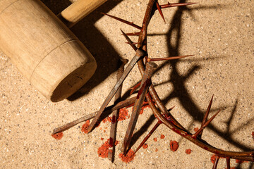 Crown of thorns with nails, mallet and blood drops on sand