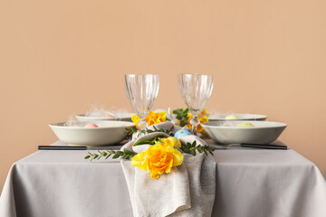 Stylish table setting with floral decor for Easter celebration near color wall