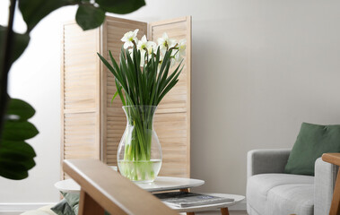 Vase with daffodils on table in light living room