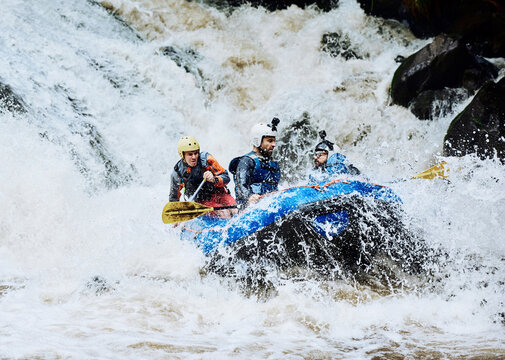 We asked for extreme adventure and we got it. Shot of a group of determined young men on a rubber boat busy paddling on strong river rapids outside during the day.