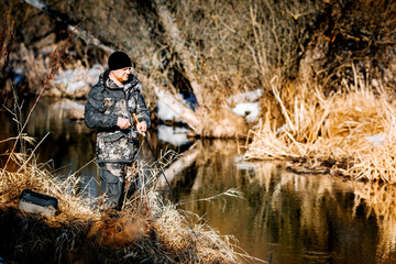 A fisherman with a fishing rod catches fish on the bank of a snow-covered river in early spring